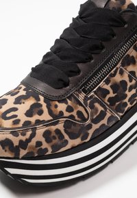 Sneakers w wzór lamparta z czarnymi sznurowadłami, akcentami z ekoskóry oraz masywną białą i czarną paskową podeszwą. Posiadają boczny zamek.