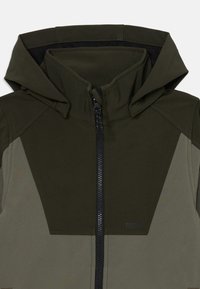 Green jacket with a hood, featuring a zip closure, contrasting lighter green panels, and a soft, textured fabric. Notable triangular design accents.
