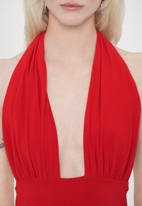 Červené plavky na halterneck s hlbokým V-výstrihom a drapériou v látke. Hladký materiál s naberanými detailmi okolo výstrihu.