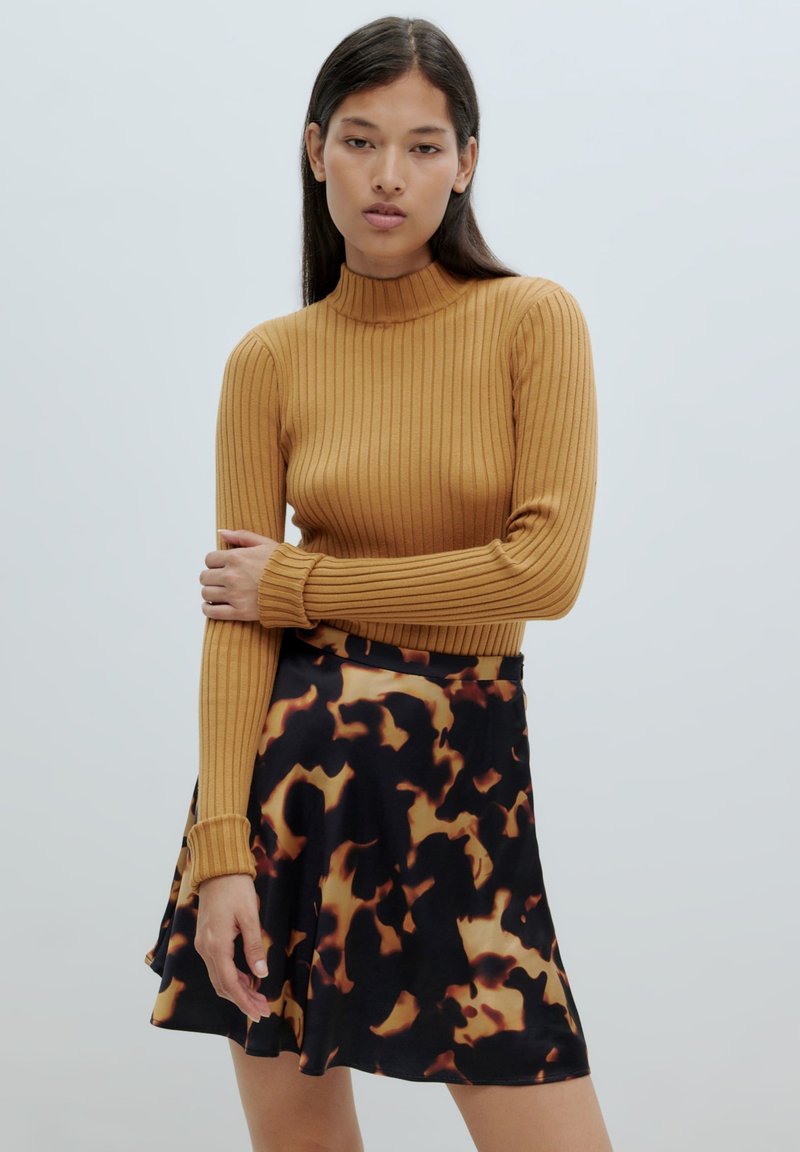 Rippstrick Senfgelber Rollkragenpullover mit langen Ärmeln, kombiniert mit einem schwarzen Rock mit einem braunen abstrakten Muster. Geschmeidiger, leichter Stoff.