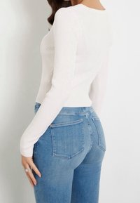 Biały, prążkowany top z długim rękawem w połączeniu z niebieskimi dżinsami o wysokim stanie, posiadającymi gładkie wykończenie, dwie tylne kieszenie i lekki stretch.