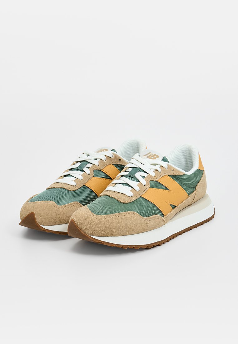 Zapatillas verdes y marrones con acentos amarillos, materiales de malla y ante, cordones blancos y una suela de goma texturizada. Diseño clásico con un logo prominente.