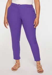 Fialové slim-fit kalhoty s hladkým povrchem, vybavené zapínáním na knoflík a poutky na opasek. V kombinaci se světlými sandály na řemínky.