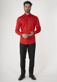 Rode langwerpige shirt met zwarte patroonaccenten, witte knopen en een fitted ontwerp. Gecombineerd met zwarte broek en zwarte schoenen.