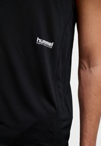 Zwart mouwloos prestatiek shirt met een gestructureerde stof, witte "hummel PERFORMANCE" logo op de borst, en versterkte stiksels.