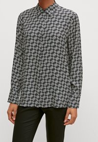 Chemise à motifs noir et blanc avec col, manches longues et coupe décontractée. Présente un design géométrique et des boutons.