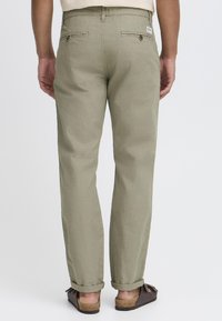 Pantalons en mélange coton vert clair, coupe droite, avec des revers, des poches arrière et une petite étiquette de marque près de la taille.