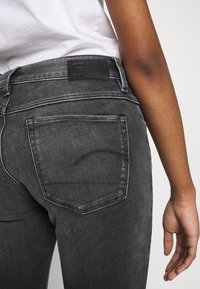 Černé dž íny z denimu s mírně vybledlou texturou, vybavené zadními kapsami, koženou štítkem na pásku a kontrastními švy.