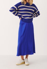 Blauwe gestreepte gebreide trui met beige strepen, gecombineerd met een effen blauwe satijnen rok en witte sneakers met gele zolen.