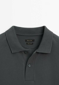 Polo gris foncé avec un col plié et deux boutons, montrant l'étiquette de la marque "Massimo Dutti" et les étiquettes "Made in Turkey" à l'intérieur du col.