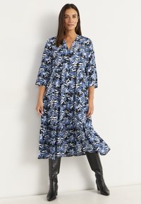Blumengemustertes Kleid in Blau und Schwarz mit V-Ausschnitt und drei Viertelärmeln, das einen weit auslaufenden Saum und ein schichtetes Design aufweist.
