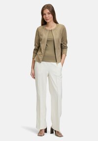 Beige suede zip-up jacket over een groene top, gecombineerd met witte hoge taille broek en groene hakken. Minimalistisch design en strakke lijnen.