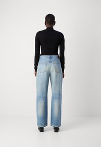 Un haut noir à manches longues associé à un jean ample bleu clair, avec une taille haute et des poches arrière visibles. Denim texturé avec une finition délavée.