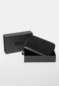 Black leather wallet with a zip closure, inside a black cardboard box featuring the brand logo. Smooth texture and rectangular shape.