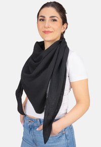 Écharpe noire faite de tissu texturé, drapée lâchement autour du cou. Elle a une forme triangulaire avec des bords bruts et des motifs en grille subtils.