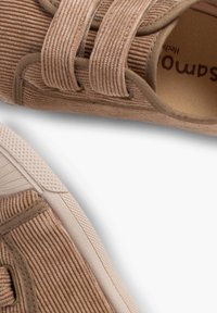 Baskets en corduroy beige avec deux fermetures en bande, semelles en caoutchouc et détails de surface texturés. Design minimaliste avec une forme arrondie.