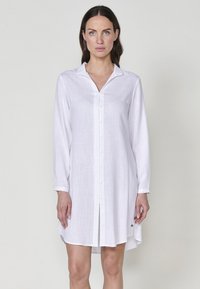 Rochie albă, cu mâneci lungi, din bumbac, cu guler în V și crăpături laterale. Prezintă un mic accent al mărcii aproape de tiv.