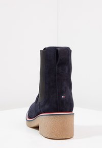 Semišové kotníčkové boty v námořnické modři s texturovaným povrchem, elastickými bočními panely a rozšířeným sv�ětle zbarveným gumovým podpatkem s červenými a modrými akcenty.