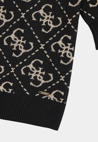 Czarny sweter z dzianiny z powtarzającym się beżowym wzorem i ściągaczami. Zawiera małą metalową metkę z logo 'GUESS' z boku.