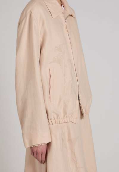 Beige jacket with floral embroidery, front zipper, collar, elastic waistband, and a matching skirt worn by a person against a plain background.