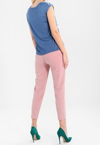 Modrá krátká košile s květinovým vzorem na ramenech, zkombinovaná s růžovými slim kalhotami a zelenými lodičkami. Jednoduché pozadí.