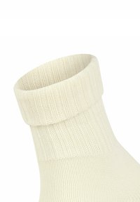Calzino lavorato a maglia di colore crema con una texture a coste e un polsino piegato alla caviglia, che mostra un design accogliente e un materiale morbido.
