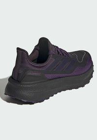 Chaussure de sport noire et violette avec tige en mesh, semelle rembourrée et accents texturés. Présente trois rayures caractéristiques et un logo "ULTRABOOST".