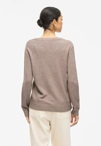 Pull en laine brun à la coupe décontractée, avec des manches longues et un ourlet côtelé, associé à un pantalon large de couleur crème.