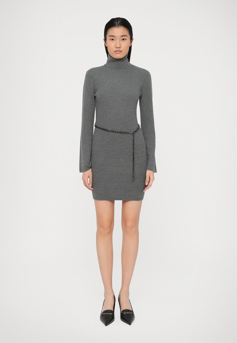 Grå ribbet turtleneck kjole med en tætsiddende silhuet, der har lange ærmer og et sort kædebælte i taljen. Sorte spidse sko.
