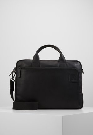 Sacoche en cuir noir avec deux poignées, une sangle amovible et une fermeture éclair. Présente des coutures minimales et un logo extérieur.