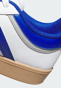 Zapatilla blanca con acentos azules y tejido texturizado. Parte superior de cuero liso con costuras en contraste y suela de goma texturizada.