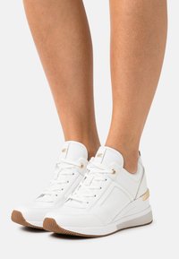 Hvit lær sneakers med gullakenter, med et strukturert mønster og en tykk gummi såle. Snøring med metallevender gir en sikker passform.