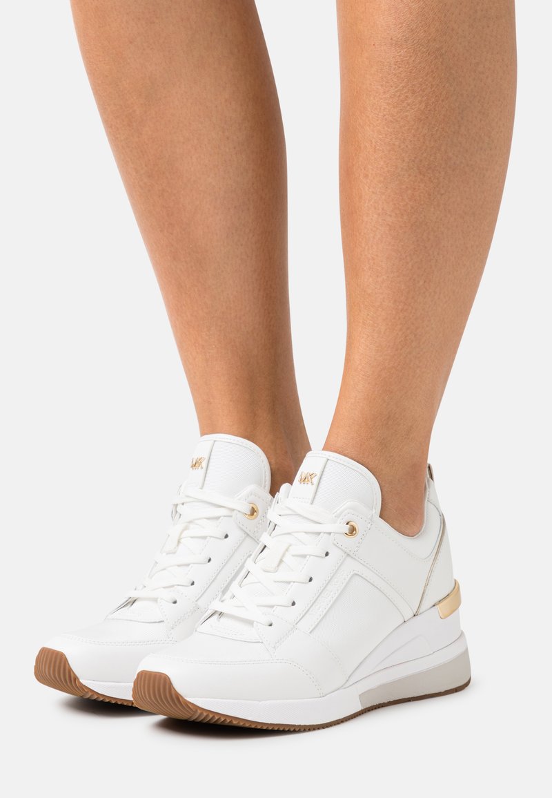 Hvit lær sneakers med gullakenter, med et strukturert mønster og en tykk gummi såle. Snøring med metallevender gir en sikker passform.