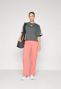 Dark gray cropped t-shirt with white logo, paired with bright pink sweatpants. Model carries a black shoulder bag, wearing white sneakers.