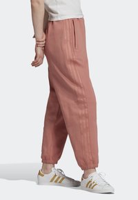 Rosa mjukisbyxor med avslappnad passform, elastiska muddar och sidofickor, med tre vertikala ränder längs de yttre sömmarna.