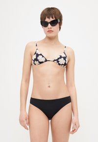 Fekete virágmintás bikini felső vékony pántokkal, fehér és világos rózsaszín virágokkal díszítve. Fekete bikini alsó sima felülettel. Fekete macskaszem napszemüveg.
