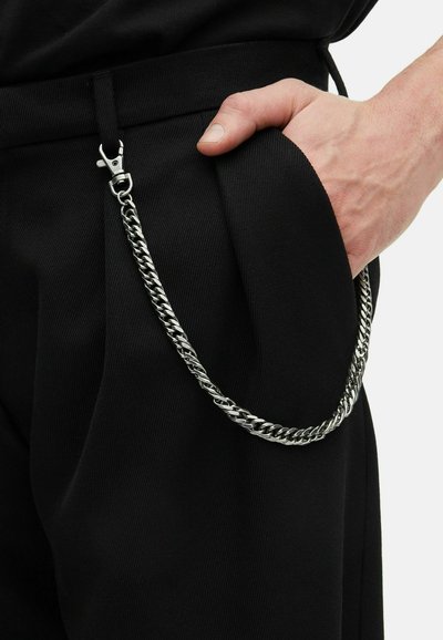 Pantalones negros con un diseño plisado, que cuentan con una cadena plateada sujeta a un clip en la cintura, destacando una tela texturizada.