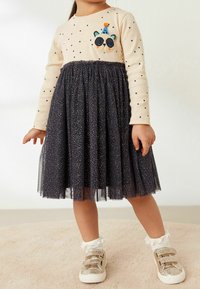 Haut beige à manches longues avec des pois noirs et une patch de panda, associé à une jupe en tulle navy ornée de petits éclats d'or.