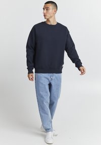 Felpa blu navy con maniche lunghe, scollatura rotonda e polsini a costine. Abbinata a jeans della giusta vestibilità blu chiaro e sneakers bianche.
