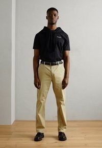 Zwarte korte mouwen hoodie met trekkoord, beige chino's, zwarte riem en zwarte schoenen. Glad stof, neutrale tinten en een ontspannen pasvorm.