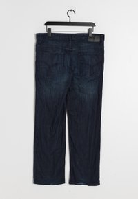 Jeans de mezclilla azul oscuro con corte recto, que cuentan con dos bolsillos traseros y una parche de cuero en la cinturilla. Detalles de desvanecimiento mínimos.