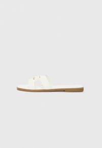 White flat slide sandal with a minimalist design, featuring two crossed straps and gold-tone hardware accents on a brown sole.