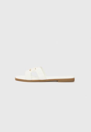 White flat slide sandal with a minimalist design, featuring two crossed straps and gold-tone hardware accents on a brown sole.