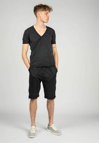 Sort kortærmet V-hals T-shirt med et unikt draperet design, parret med sorte denimshorts og lyse sneakers.