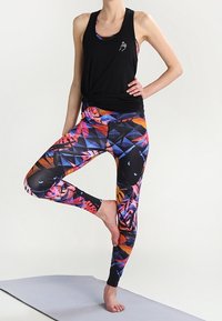Black tank top with a knot detail, paired with colorful leggings featuring geometric and floral patterns in pink, orange, and blue tones.