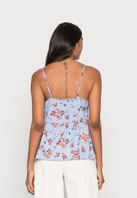 Top de alças spaghetti azul floral com design peplum, apresentando flores cor-de-rosa e vermelhas sobre um fundo azul claro. Tecido suave e leve.