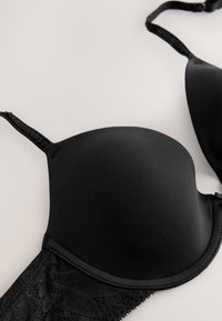 Schwarzer gepolsterter BH mit Spitzen-Details und verstellbaren Schulterträgern auf hellem Hintergrund.