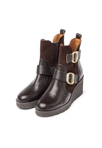 Botas marrones hasta el tobillo con un acabado de cuero texturizado, acentos de ante, cremallera lateral y una correa ajustable con hebilla en la parte superior. Diseño de suela de cuña.