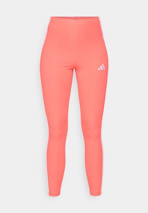 Koraal kleurige sportleggings gemaakt van rekbaar materiaal, met witte zijkanten en een klein wit logo op de bovenste linkerkant.