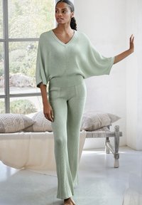 Lichtgroene gebreide co-ord-set met een V-hals top met brede mouwen en aansluitende, flared broeken met ribbeltextuur en subtiele naaddetails.
